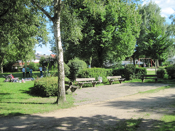 Zwei Bänke neben einem Baum im Hintergurnd grüne Wiesen des Parks am Entenweiher