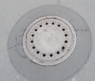 Großer runder Schachtdeckel eingelassen im Straßenasphalt.
