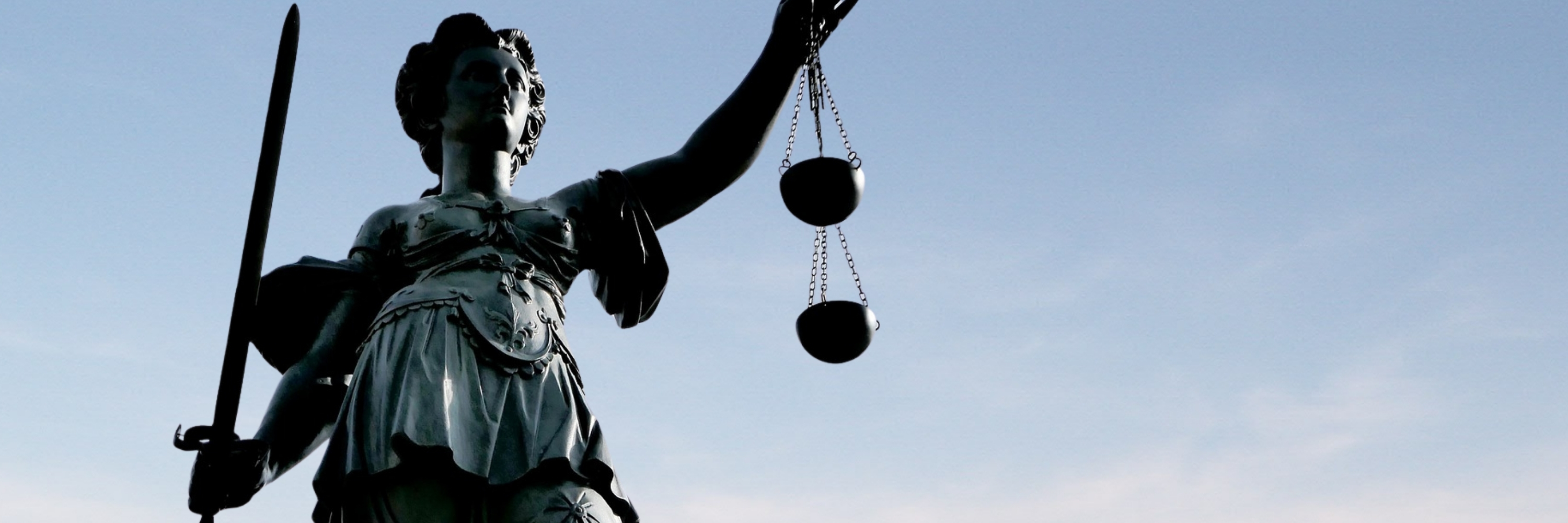 Statue der Justitia mit Waage in der rechten und Schwert in der linken Hand vor blauem Himmel