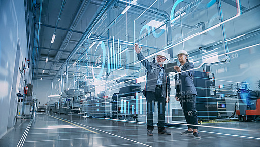 Zwei Personen mit Schutzhelmen in einer Fabrikhalle vor digitalen Grafiken und Diagrammen