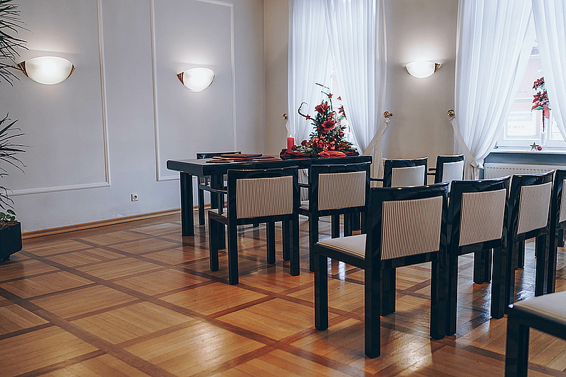 Blick auf das Trauzimmer des Standesamts Rödermark, im Vordergrund die Bestuhlung für die Gäste mit schwarz-weißen Stühlen, im Hintergrund der festlich mit Blumen geschmückte Tisch, an dem das Brautpaar Platz nimmt.