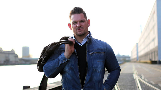 Florian Sitzmann mit blauer Jacke im Rollstuhl sitzend an einer Kaimauer.